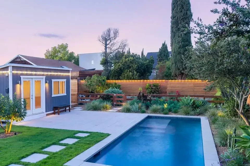 Backyard in-ground pool with sandstone paving surround and a timber-clad cabana at dusk