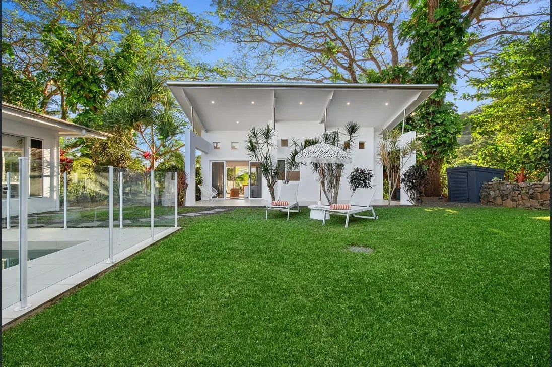 Backyard pool edge with glass fencing, sun loungers and umbrella beside a large lawn