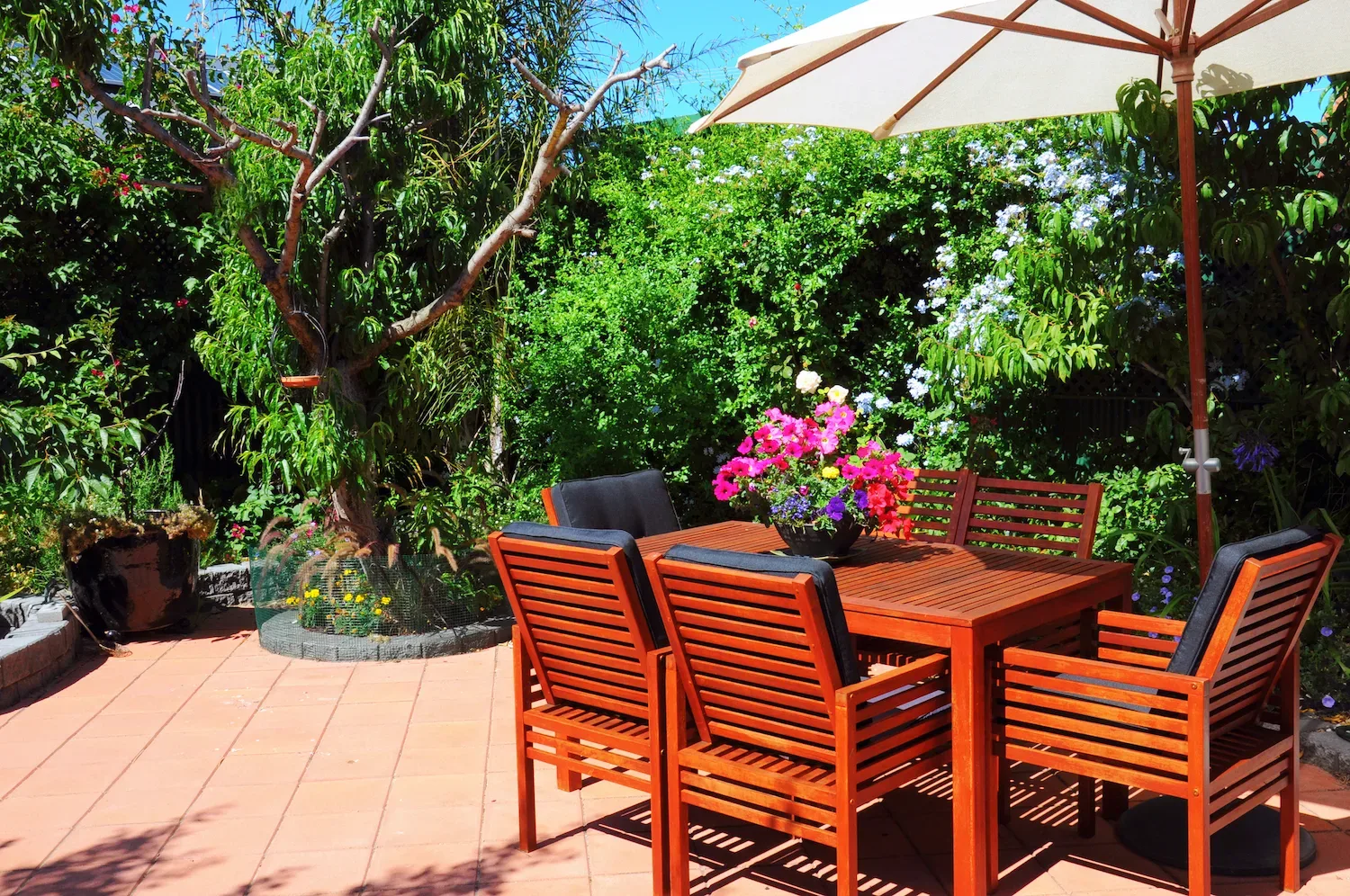 Sunny paved courtyard patio with a timber outdoor dining table and a large market umbrella